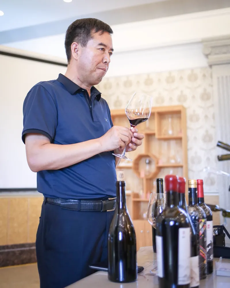 A winemaker showing glasses of red wine beside bottles at a tasting