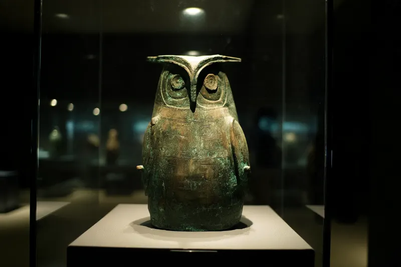 An ancient owl-shaped bronze vessel in a museum case