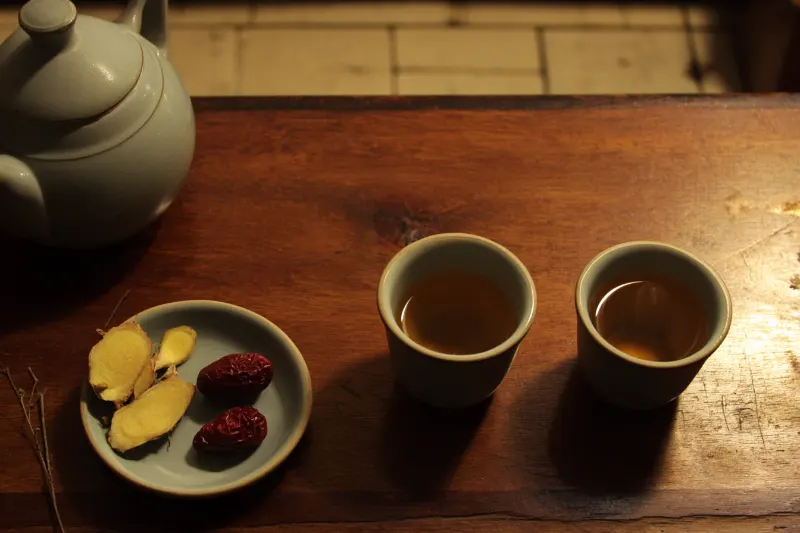 Warm Ginger Huangjiu: warm rice wine in small ceramic cups with ginger slices and a wine pot in hot water