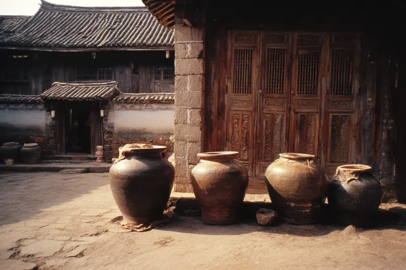 Clay wine jars in a Naxi courtyard with carved wooden doors in Lijiang