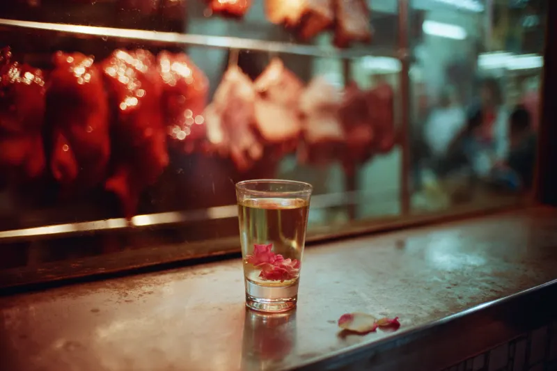 A glass of rose spirit in front of char siu pork in a Cantonese roast meat shop