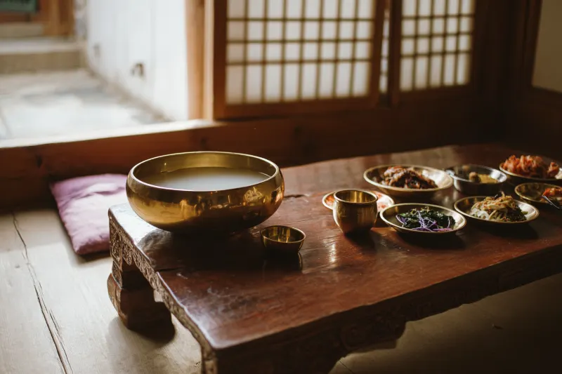 Milky and mulberry rice wine in brass bowls with Korean side dishes in Yanbian