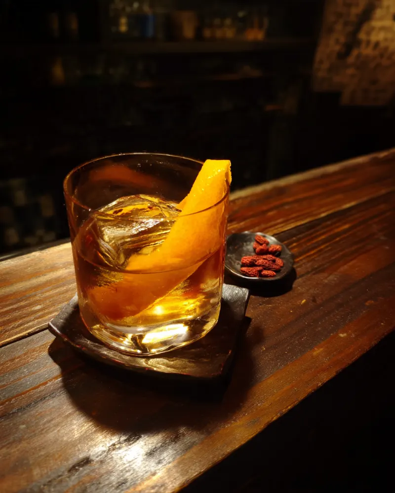 Sichuan Old Fashioned with a large ice cube, orange peel and Sichuan peppercorns