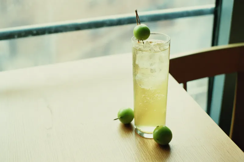 Green Plum Tonic: green plum wine and tonic in a highball glass with a fresh green plum