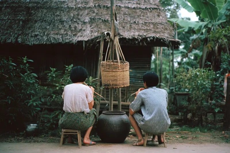 Two people sharing shanlan rice wine through bamboo tubes in a Li village, Hainan