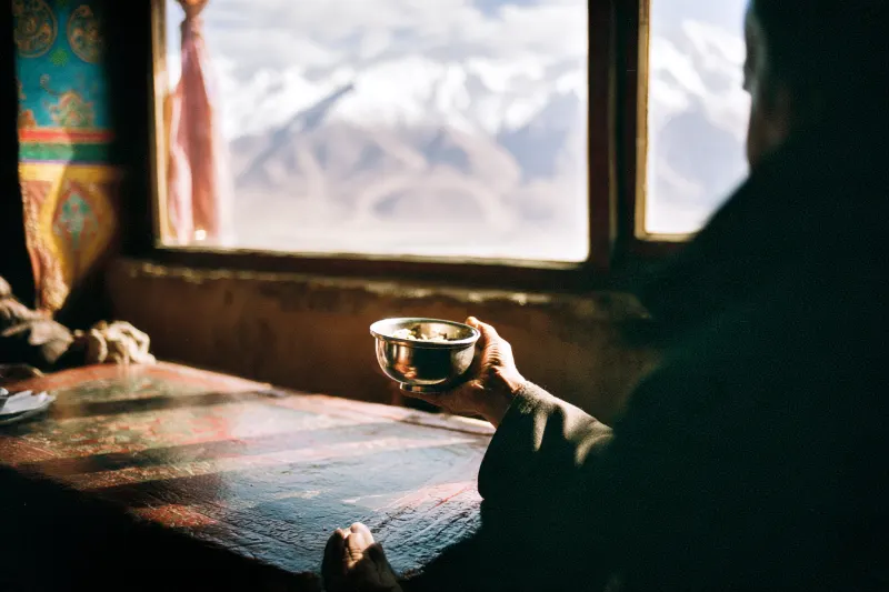 A host offering a silver bowl of barley wine to a guest in a Tibetan house